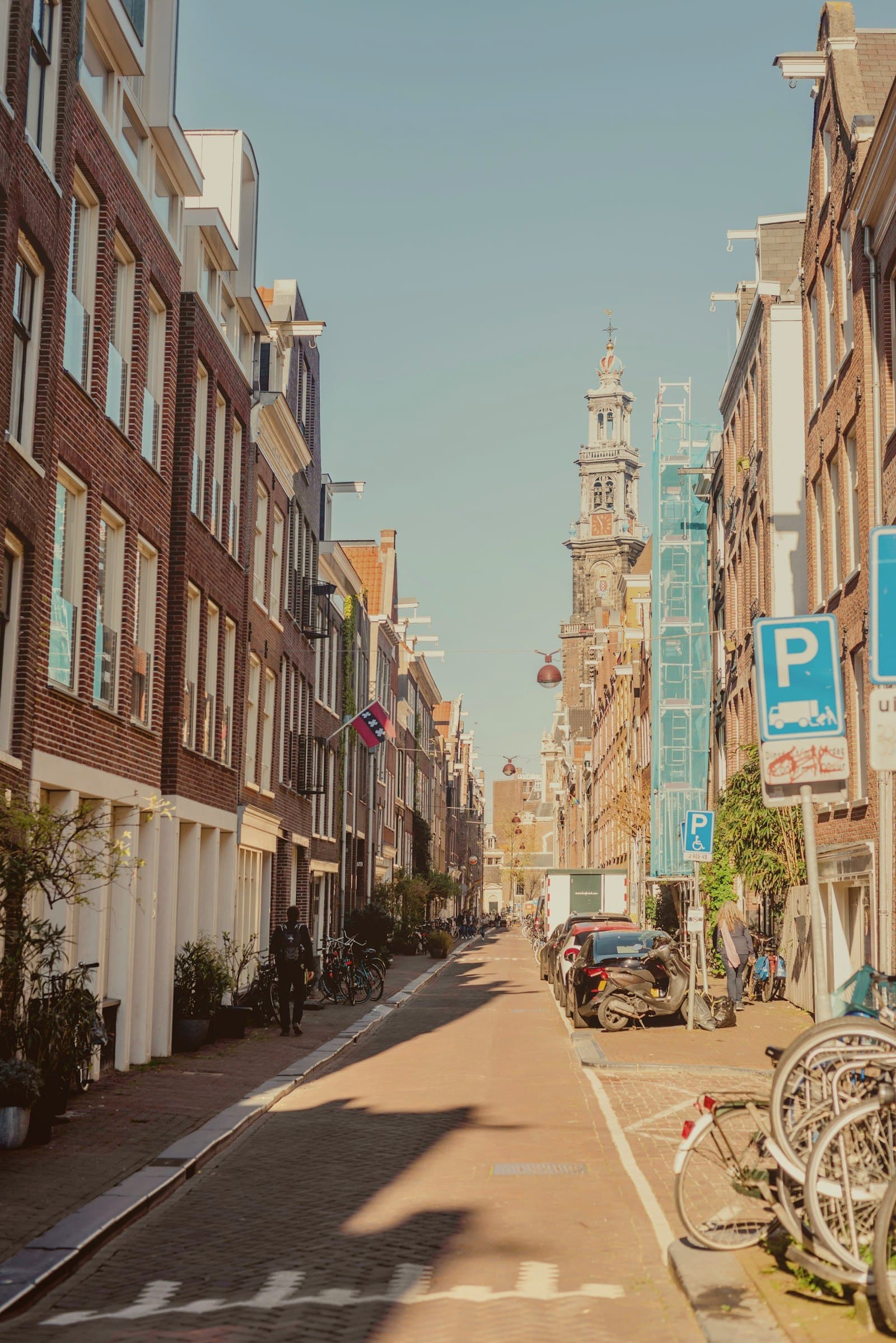 Amsterdamse straat met bakstenen gevels en een kerktoren op de achtergrond